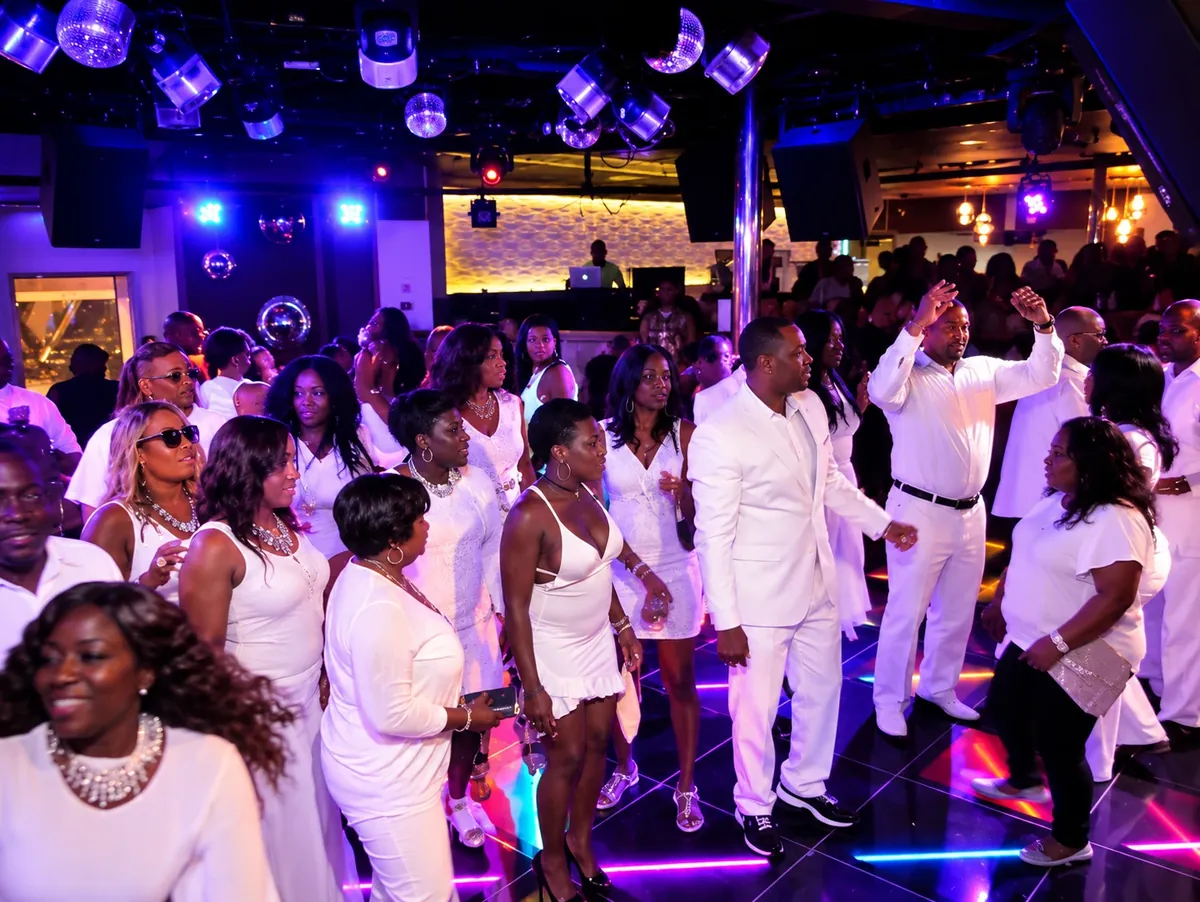 Guests in white attire dancing under colorful nightclub lights with a DJ behind the booth