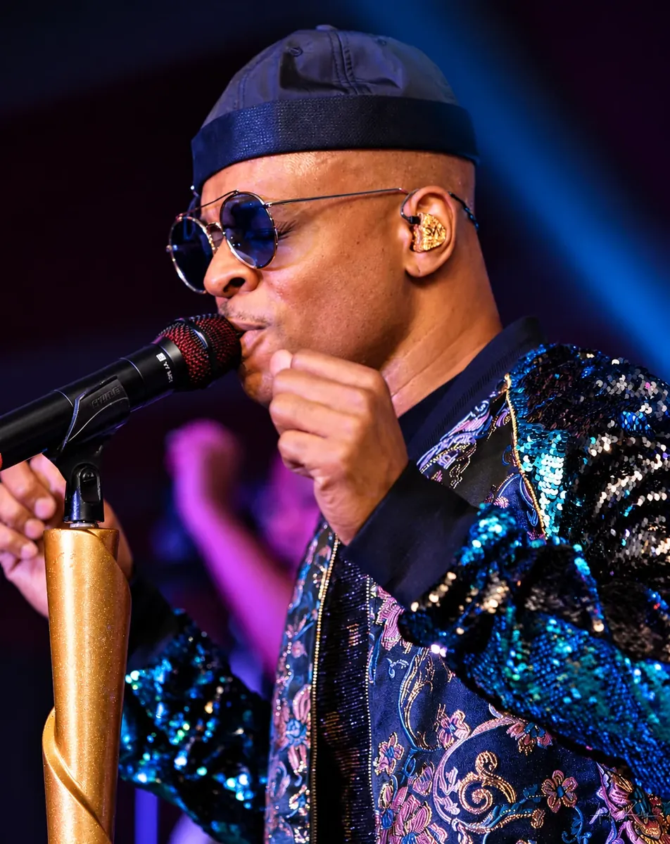Performer in a sparkling sequin jacket singing into a microphone on stage