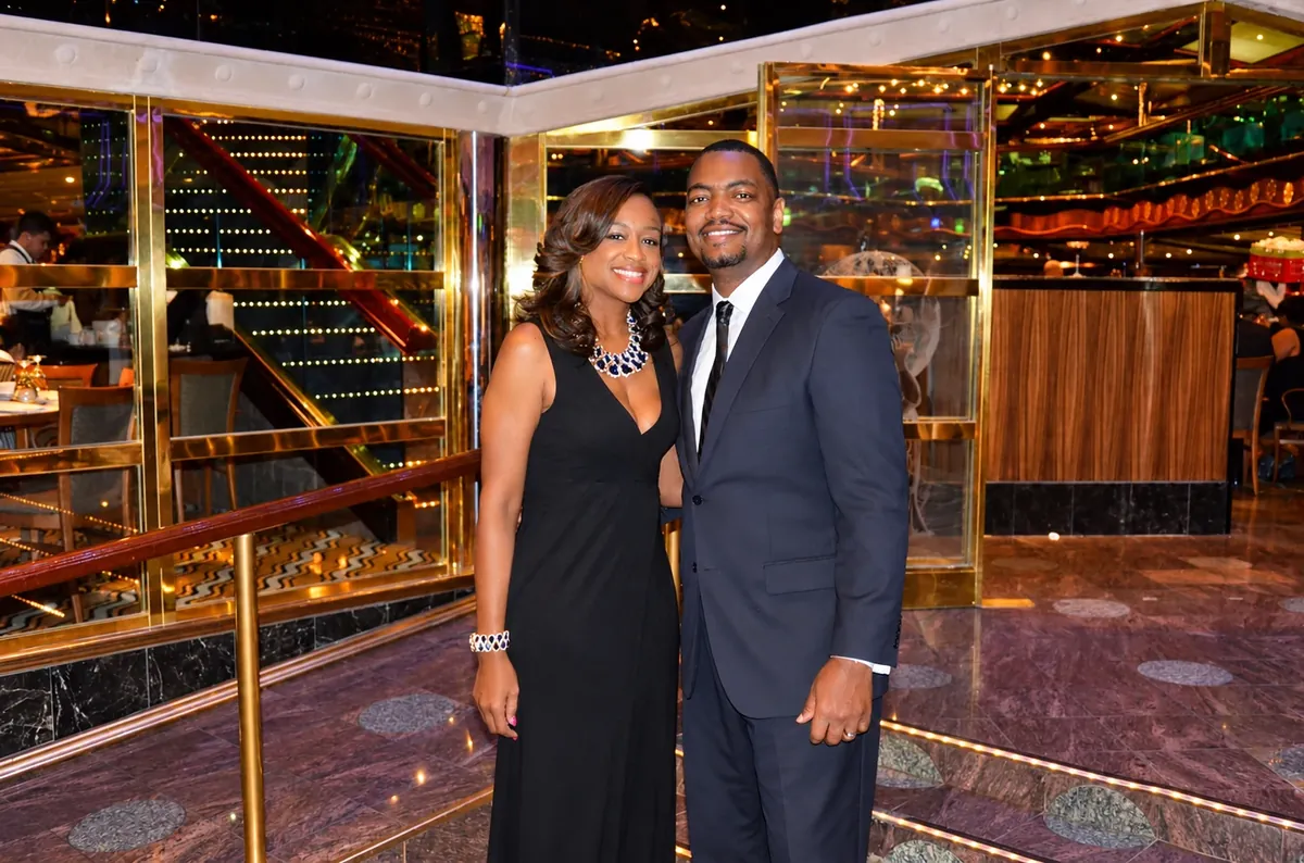 Couple in black formal attire posing beside a gold-railed staircase in a cruise ship atrium